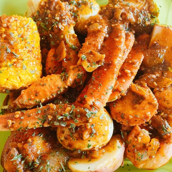 Creole seafood boil with crab legs, shrimp, corn, potatoes, and eggs, all seasoned with herbs.