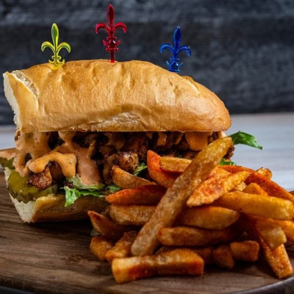 Creole 2 Geaux po'boy sandwich with fried chicken, sauce, pickles, lettuce, and a side of fries.