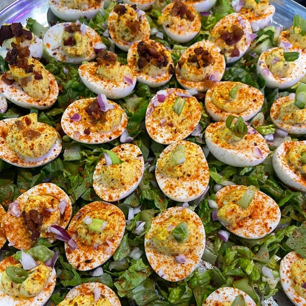 A platter of Creole deviled eggs, garnished with paprika, bacon, and green onions, on a bed of lettuce.