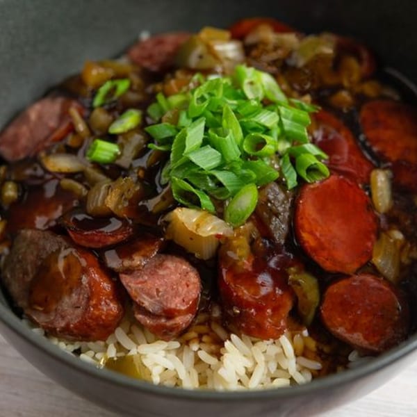 Creole 2 Geaux's dark gumbo with sliced sausage, onions, and green onions over white rice.
